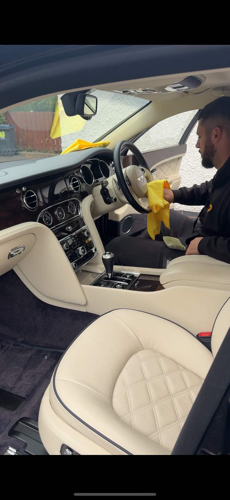 Man cleaning car interior with yellow cloth, leather seats and steering wheel.