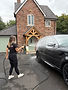 Woman power washing a black car outside a brick house