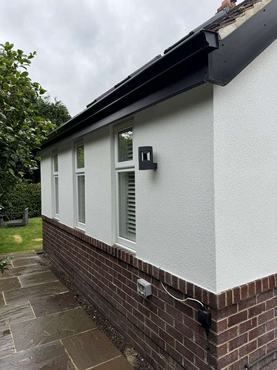 House exterior with black gutters, white render and brick base
