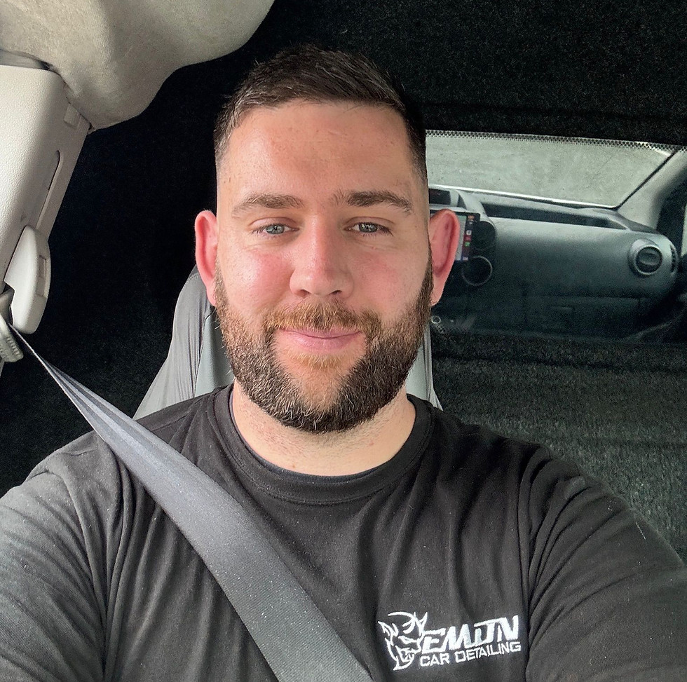 Smiling man with beard wearing black t-shirt in car
