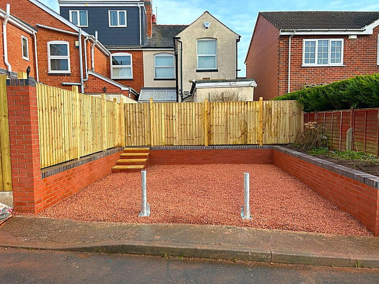 Newly installed red gravel parking area with new wooden fence and brick walls.