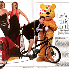 Man on tandem bike in tuxedo with three women in red and black dresses on back, and a person in a yellow bear costume. Text reads, “Let’s get this show on the road.”