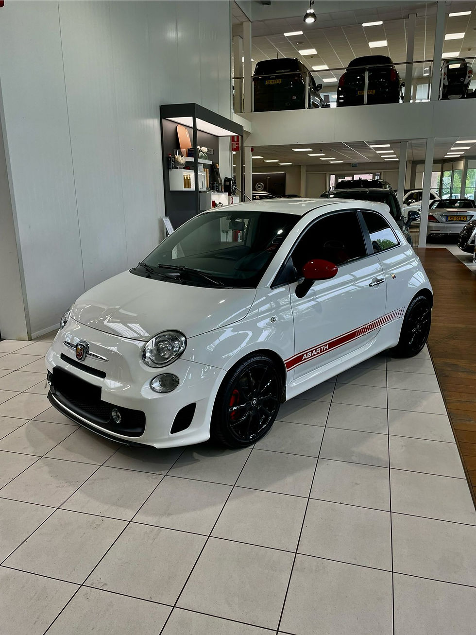 White Fiat 500 Abarth in a showroom with red stripes and black rims.