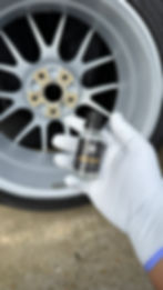 Gloved hand holds CERAMIC COATING bottle next to a car wheel.