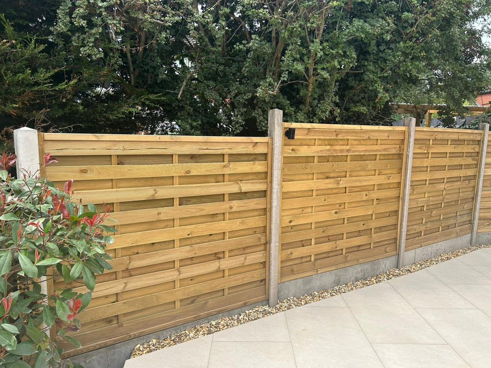 New horizontal slatted wooden garden fence with concrete posts and green trees.