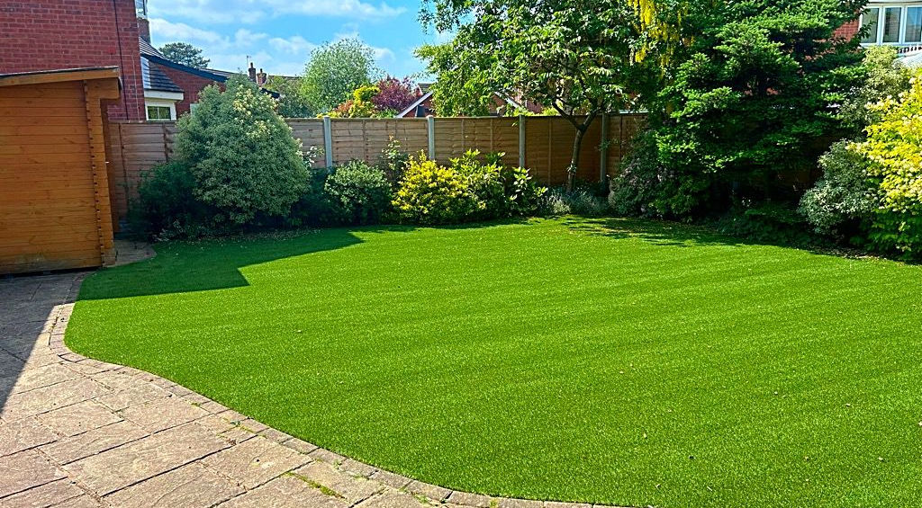 Green lawn in backyard with paving stones, trees, and fence. Kt-Landscaping.