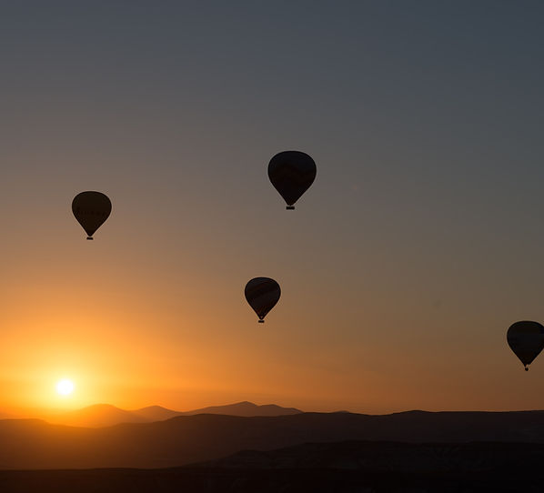 Hot air balloons flying against the sunrise over a mountain range