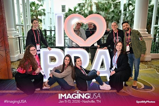 Eight people pose around a large "I ♥ PPA" sign indoors. They're smiling, with a lush greenery background. Text: Imaging USA, Jan 11-13, 2026.