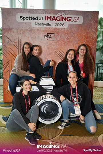 Six women pose smiling in front of a "Spotted at Imaging USA Nashville 2026" backdrop. They surround a large camera graphic indoors.