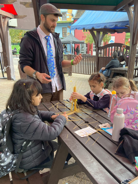 Braintastic's Mike talks to three girls seated around a picnic bench making spaghetti towers
