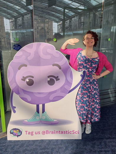 Braintastic's Ginny waves hello, standing next to Briony a large purple brain cut-out