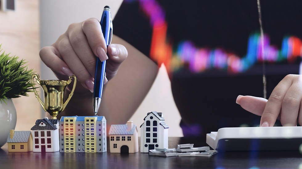 Hand holding a pen points at miniature houses beside a trophy. Another hand uses a calculator. Background shows colorful graphs.