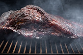 Smoke rising around a slow cooked beef brisket on the grill grates of a smoker barbecue, i