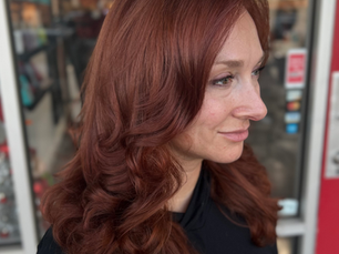 A woman with long, copper-colored hair styled in soft waves, showing warm tones and natural shine.
