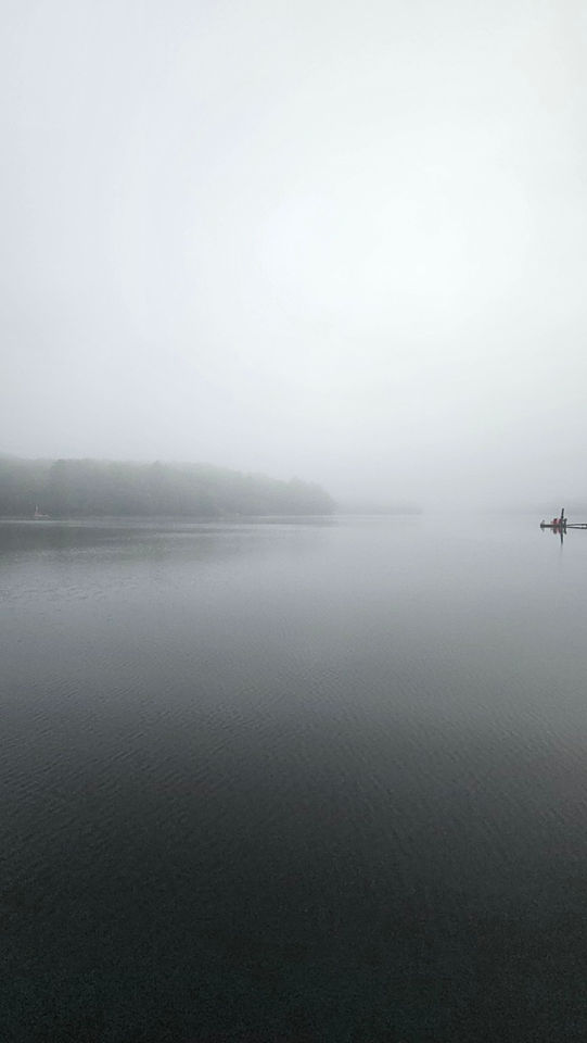 Calm misty lake with soft grey fog over the water