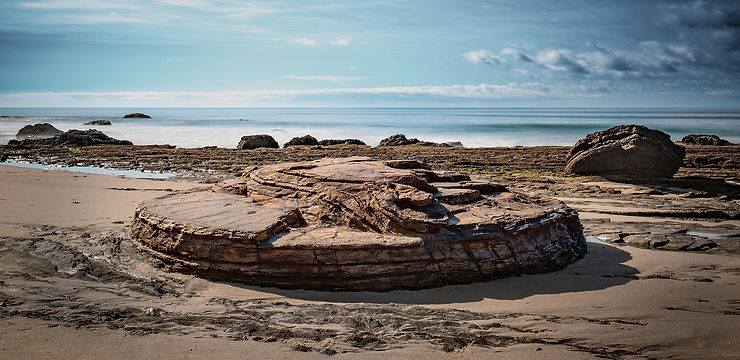 Circular dolomite concretion rock formation on Crystal Cove State Beach with ocean and blue sky with clouds in background