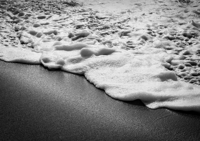High contrast close up black and white photo of soft whitewater on the sandy shore. 