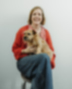 Smiling woman holding a small dog, both seated, with plain white background about them.