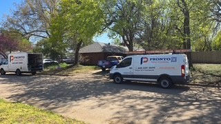 Two service vans with "Pronto" logo parked on a sunny street near trees and a house. Clear sky and green foliage create a calm scene.