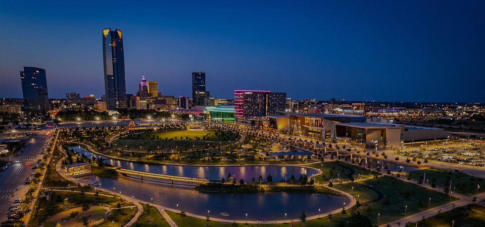 Aerial view of a city skyline at dusk with illuminated buildings, colorful lights, and a winding river in the foreground. Calm and vibrant mood.