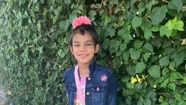 Genesis Mata taking a picture wearing a pink bow, a pink top, and a jean jacket.