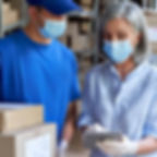 Medical courier discussing delivery details with a client in a warehouse using a digital tablet, both wearing protective mask