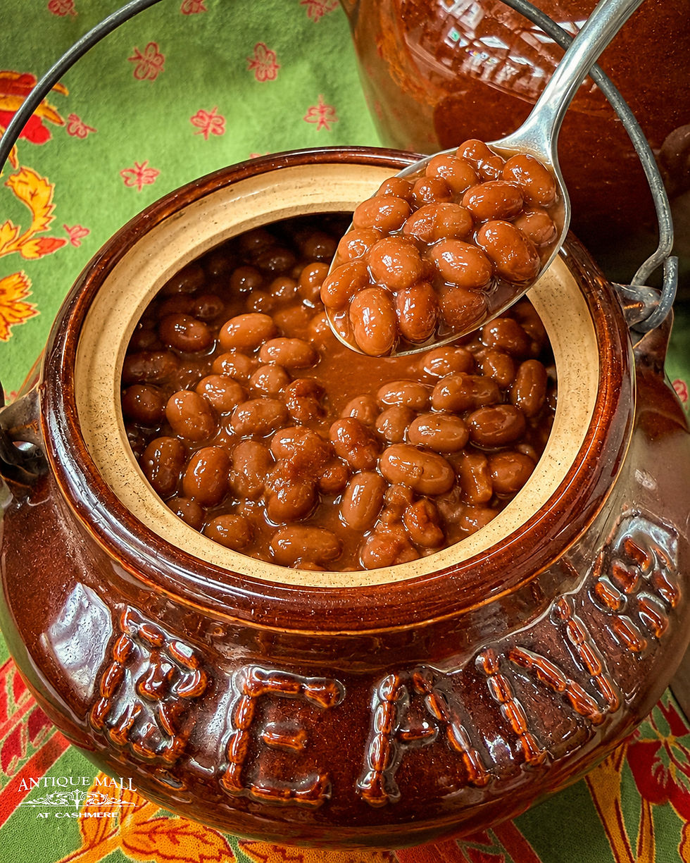 A ceramic bean pot filled with baked beans and a spoon dishing some out.