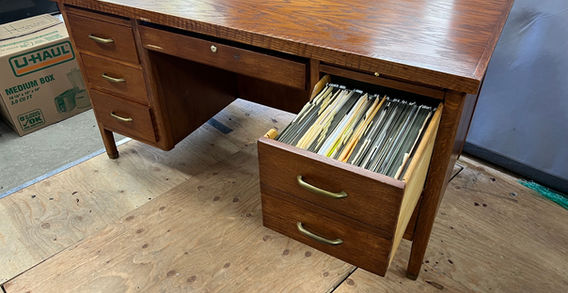 A wood desk with 7 drawers and spindle legs. Open drawers shows a file holder with files.