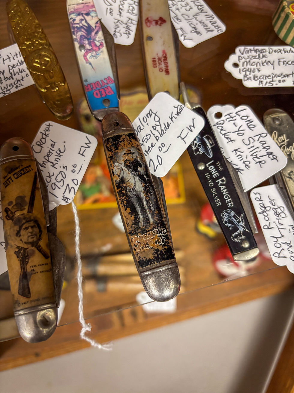 A old and faded Hopalong Cassidy child's pocket knife sits on a glass shelf with others character knives.