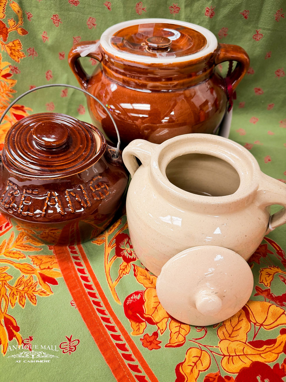 Three bean pots sit clustered on a colorful table cloth in green with red and orange florals.