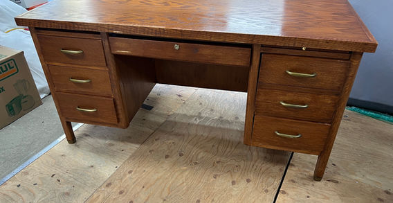 A wood desk with 7 drawers, thin metal handles, and spindle legs.