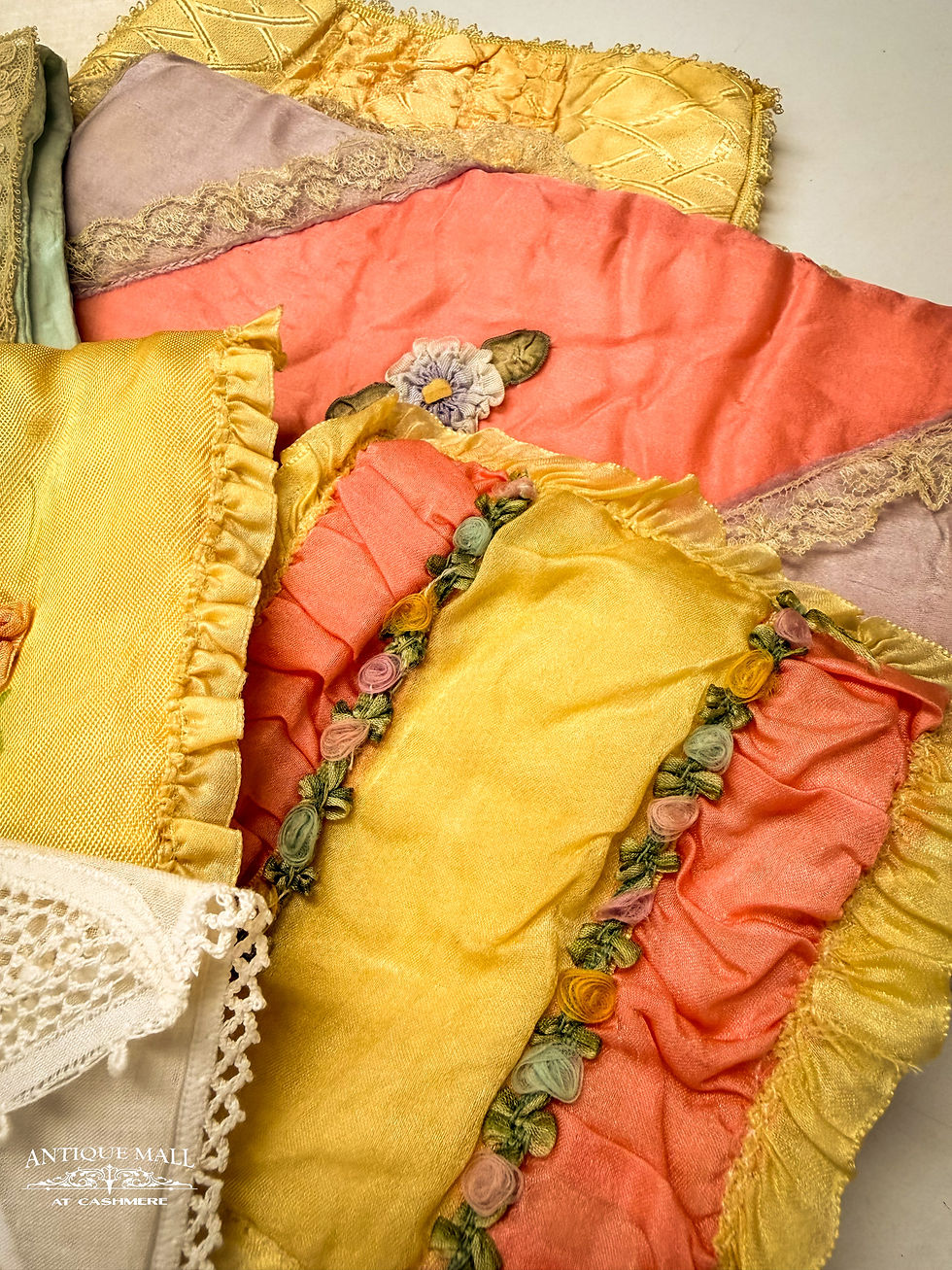 A pile of handkerchief cases with lace, ruffles, and ribbon roses decorating them.