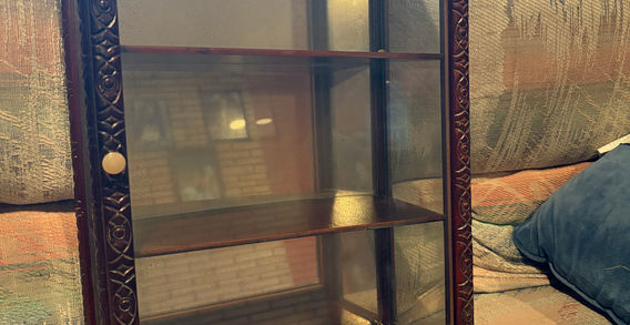 A deep colored wooden curio with glass shelves.