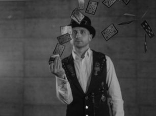 Magicien en haut-de-forme et gilet lançant un jeu de cartes en l'air, photographie en noir et blanc