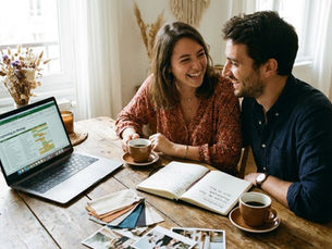 Un couple prépare le rétroplanning de son mariage sur un ordinateur portable, entouré de carnets, de nuanciers et de photos