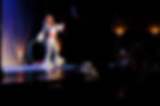 Hula hoop dancer in a silver disco suit striking a pose on stage.