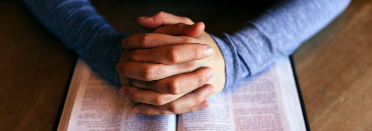 Man's hands folded over open Bible