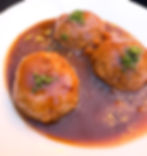 Three Liege meatballs in rich Liegeoise sauce on a white plate, garnished with chopped herbs, creating a sweet and savory flavor