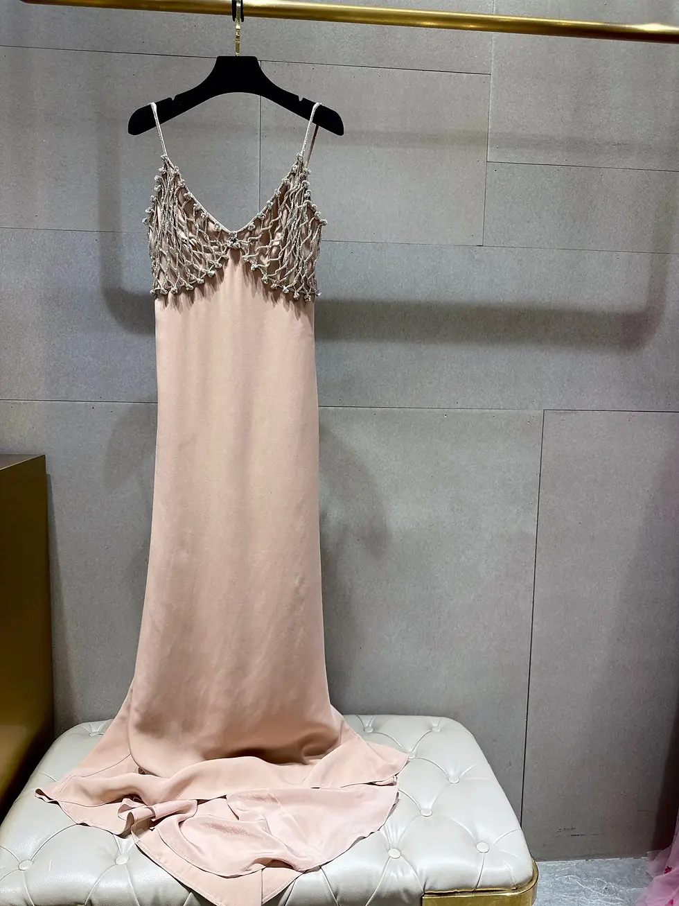 Blush pink slip dress with a delicate lace bodice hanging on a black hanger against a gray wall.