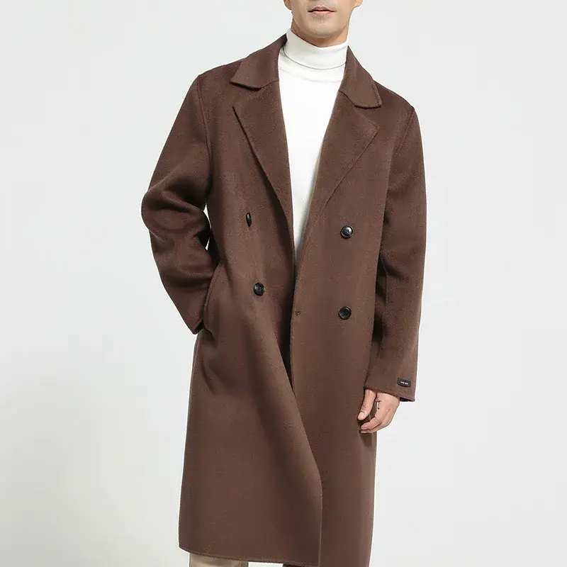 Man in a brown double-breasted coat over a white turtleneck, standing against a light background.