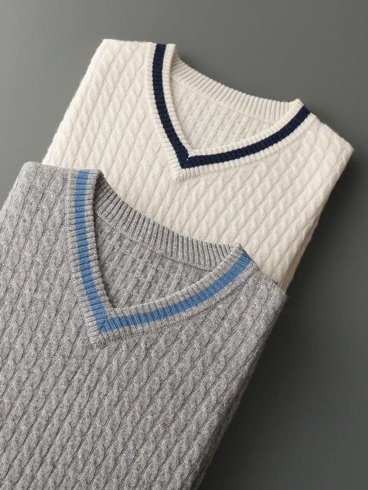 Two cable-knit sweaters, one gray with a blue trim and one white with a navy trim, on a gray surface.