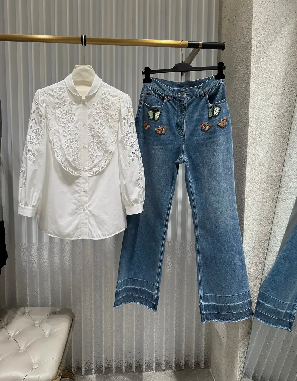 White lace blouse and blue jeans with butterfly embroidery hanging on a rail.