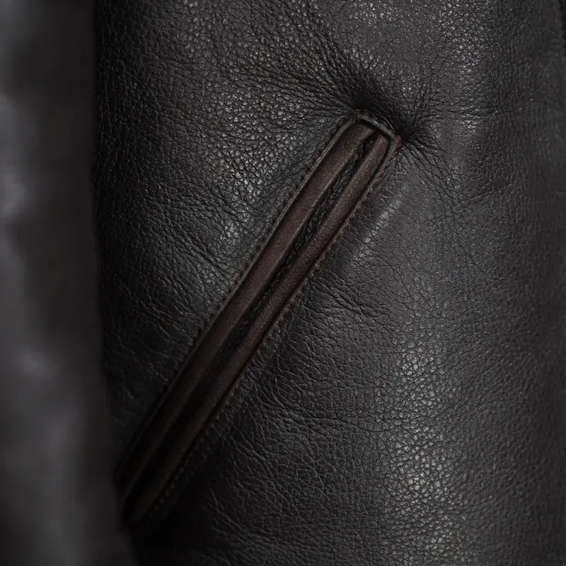 Thumbnail: Dark brown leather jacket with a plush brown collar, buttoned front, and two angled pockets, hanging in a store.