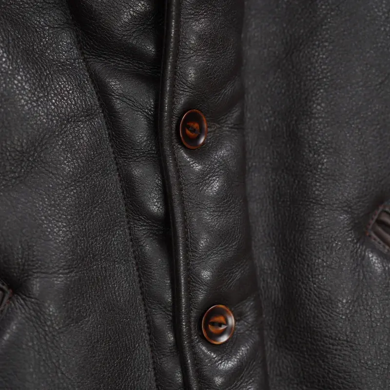 Thumbnail: Dark brown leather jacket with a plush brown collar, buttoned front, and two angled pockets, hanging in a store.