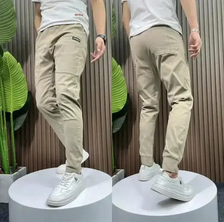 Miniaturebillede: Gray cargo pants displayed from front and back on a model wearing white sneakers and a shirt, with a striped background.