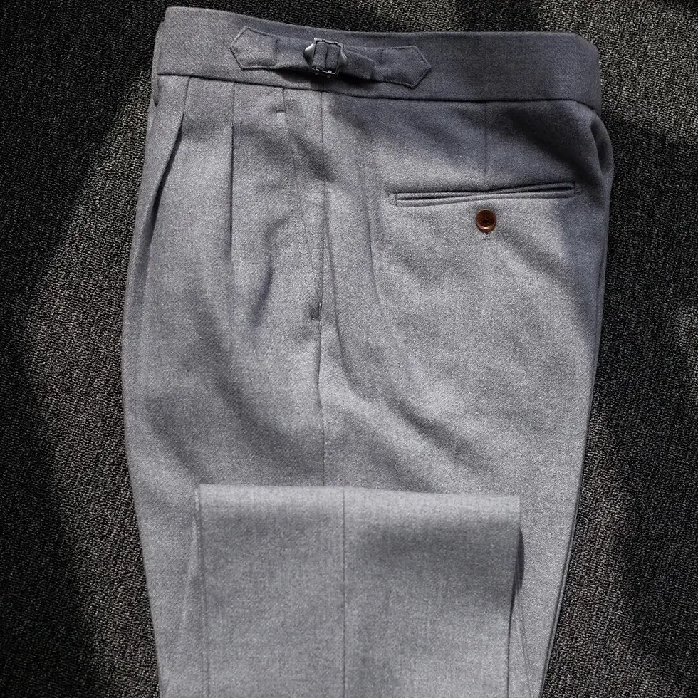 Küçük resim: Gray pleated trousers with buckle detail and pocket button, laid on dark textured surface.