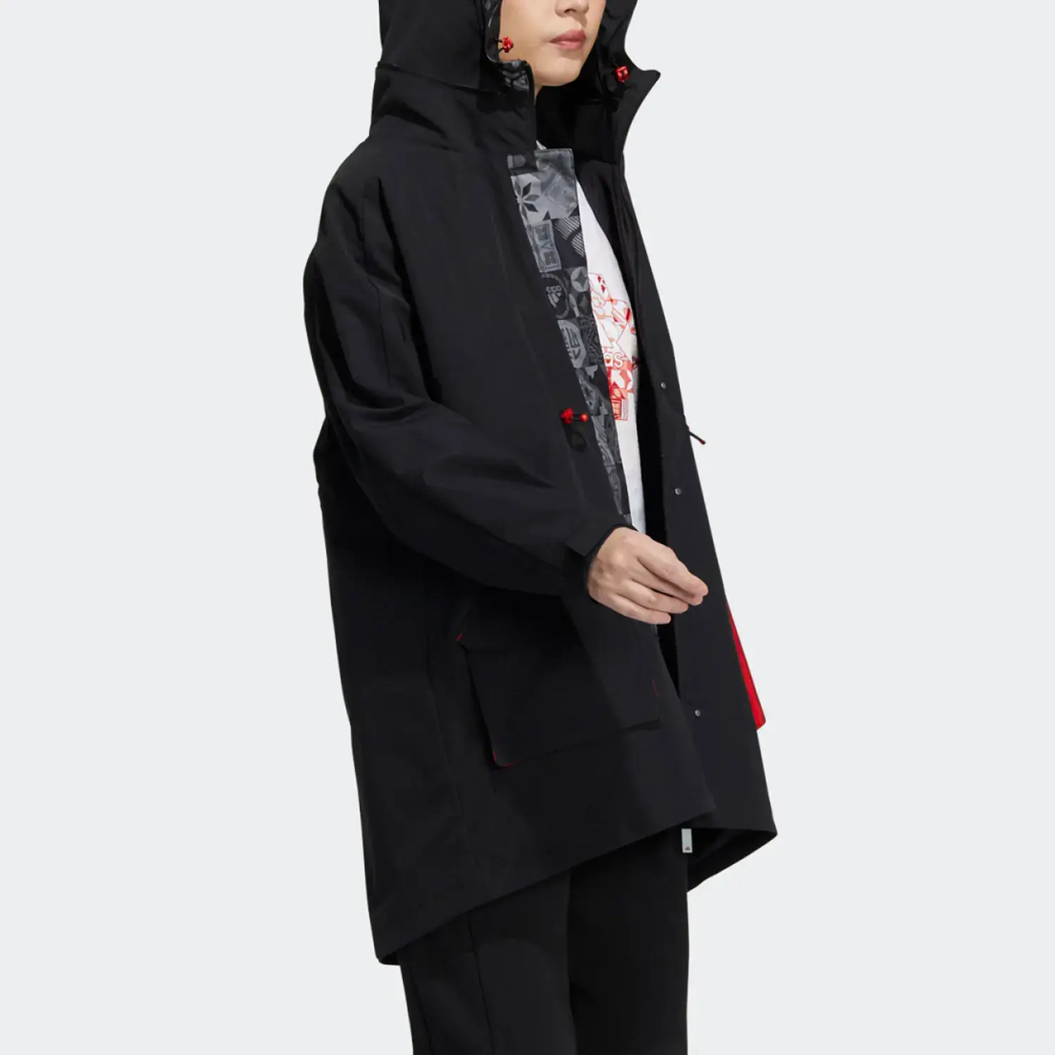 Person wearing a black hooded jacket with red accents and a graphic shirt underneath, set against a plain background.