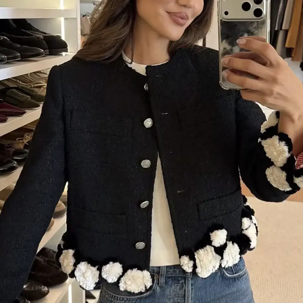 Woman wearing a black jacket with silver buttons and pom-pom details, taking a mirror selfie.