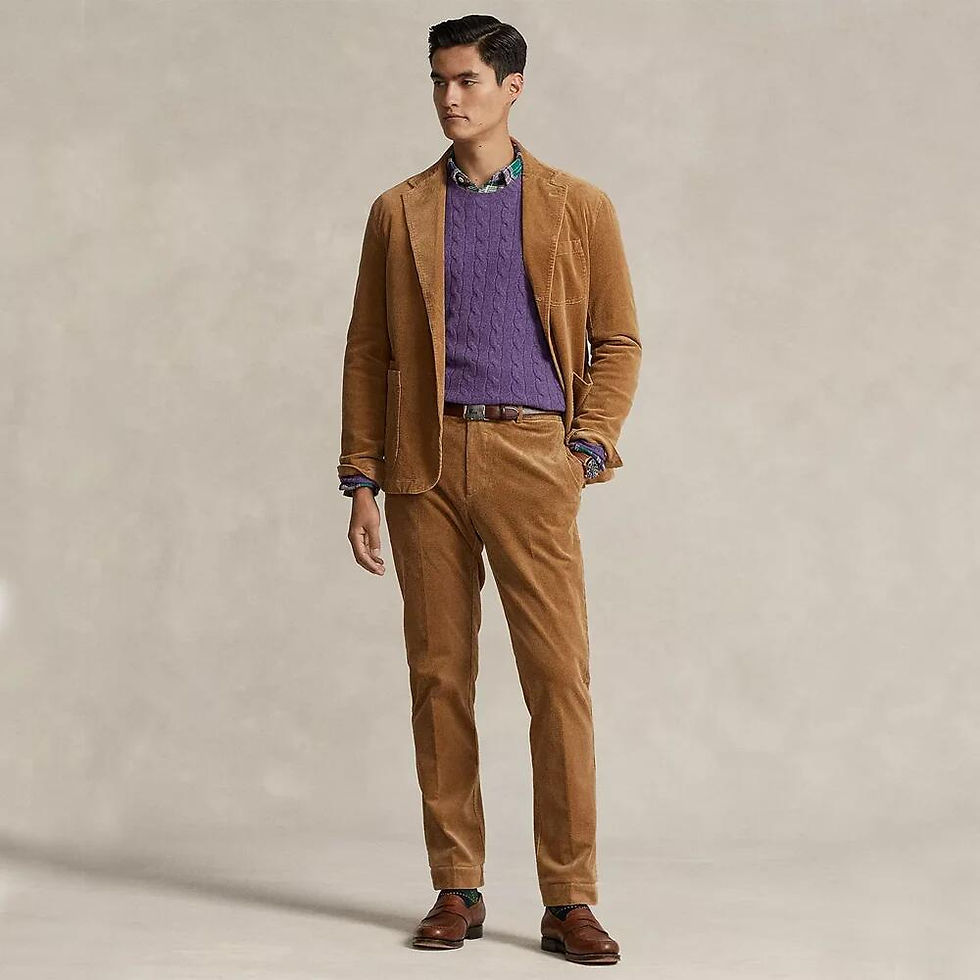 Man in tan corduroy suit, purple cable sweater, plaid shirt, and brown loafers against a neutral background.