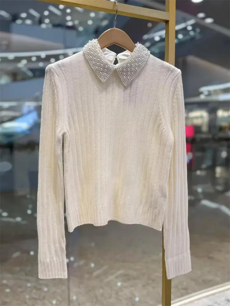 White ribbed sweater with long sleeves and a pearl-embellished collar, hanging on a wooden hanger.